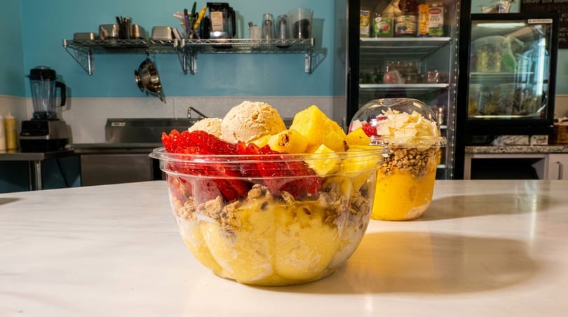 Two fruit bowls with granola, strawberries, pineapple, and ice cream on a counter.