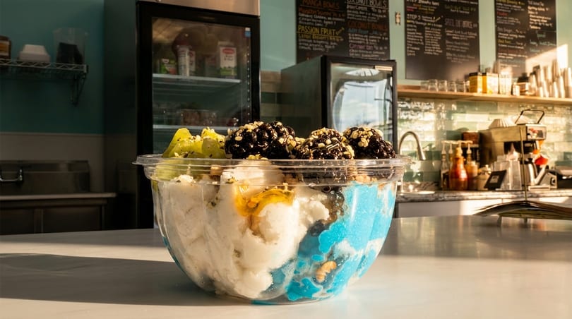 A colorful dessert bowl with white and blue ice cream, topped with kiwi, chocolate, and nuts.